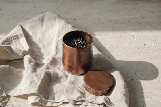 Une boîte à thé japonaise en cuivre brossé posée sur du lin naturel