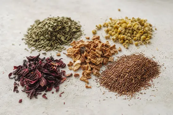 Des fleurs de camomille, des feuilles de menthe, des pétales d’hibiscus et du rooibos en petits tas