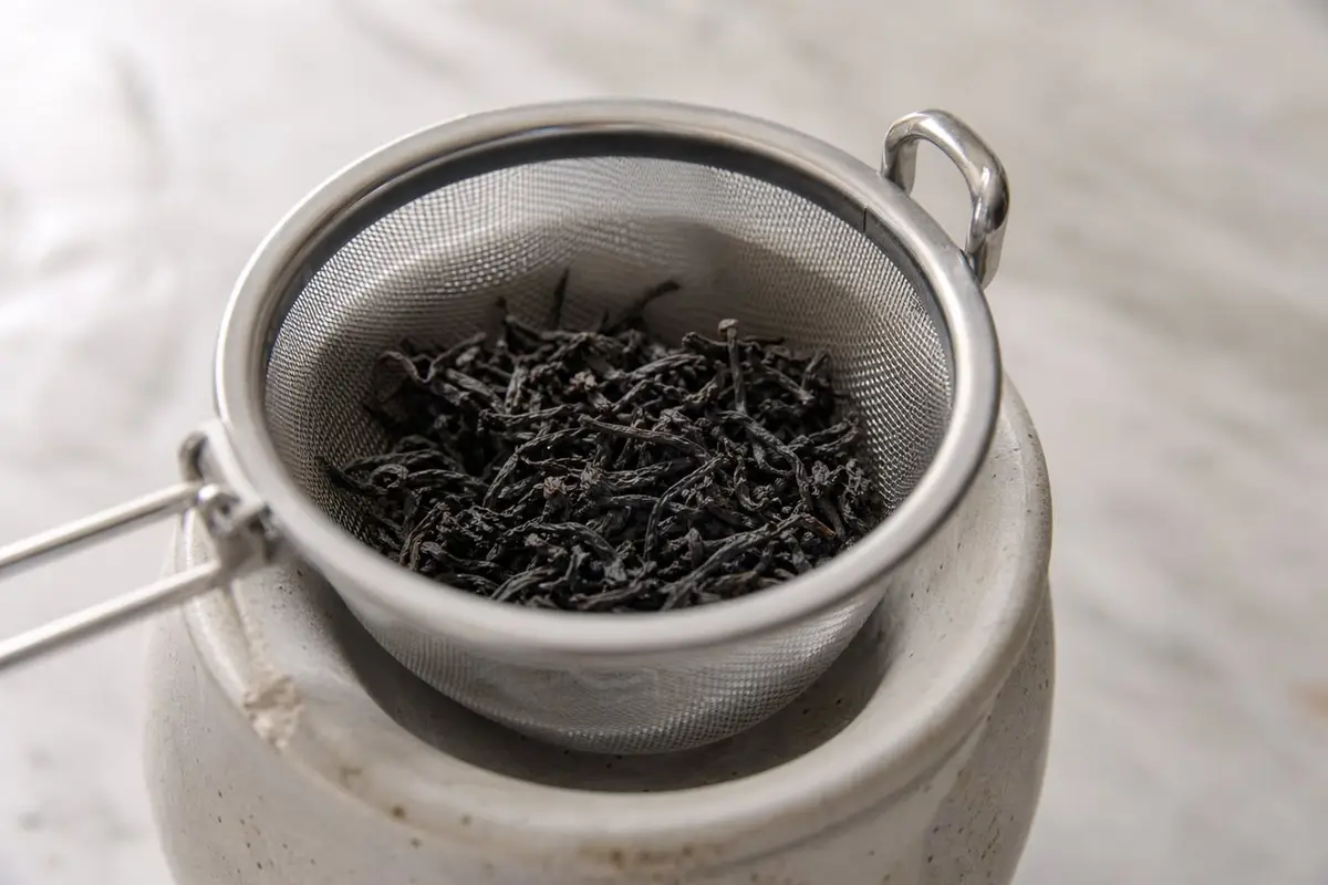 Un panier infuseur en inox rempli de thé en vrac posé sur une tasse en grès