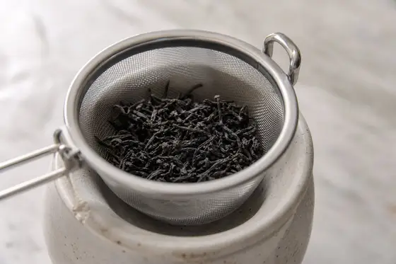 Un panier infuseur en inox rempli de thé en vrac posé sur une tasse en grès
