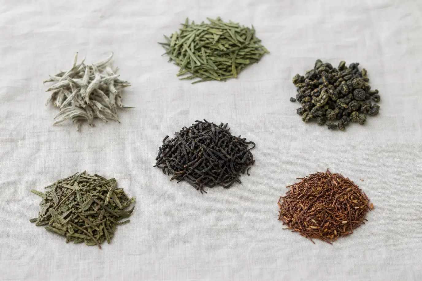 Plusieurs familles de thé en vrac, du thé blanc au rooibos, posées sur un lin clair